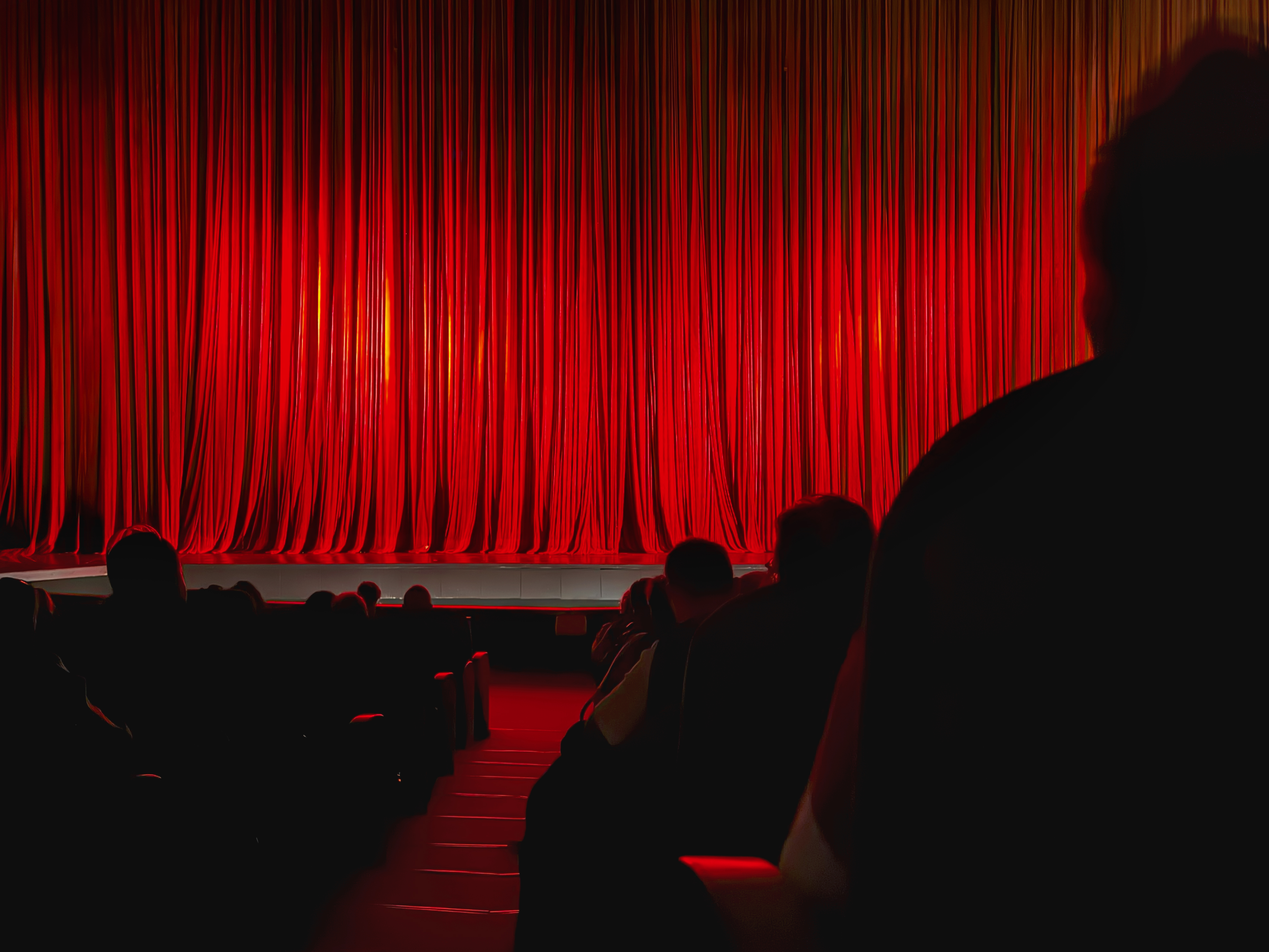 Red Theater Curtain. Closed red theater curtain illuminated by warm stage lights before performance begins. Concept of anticipation, stage performance, entertainment event
